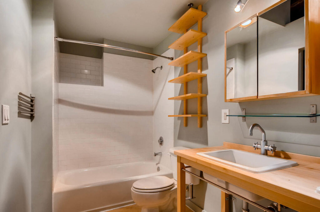 Bathroom with a mirrored wooden cabinet, shelves and a bathtub with overhead shower