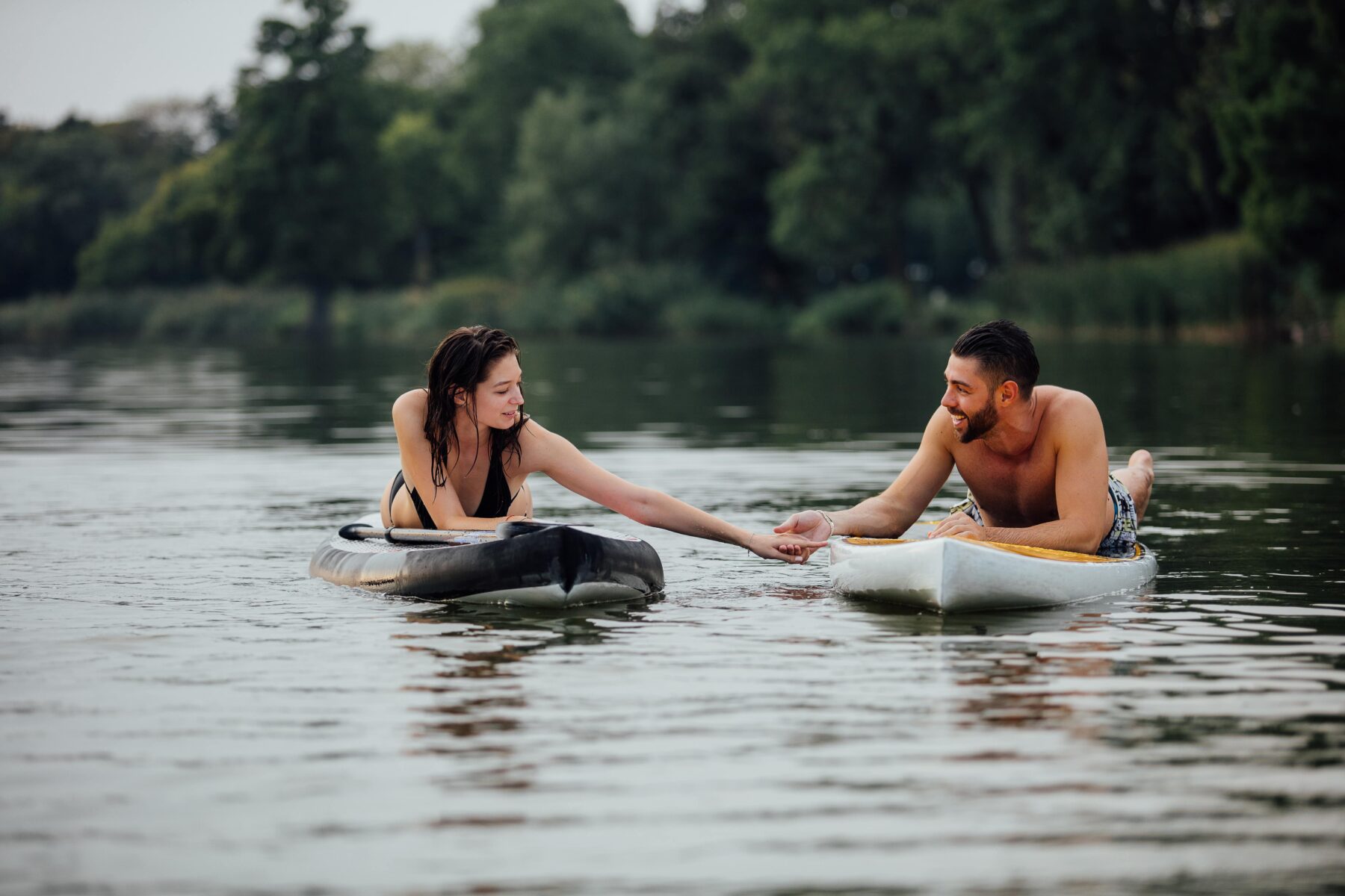 a couple holding hands while lying on paddle boards