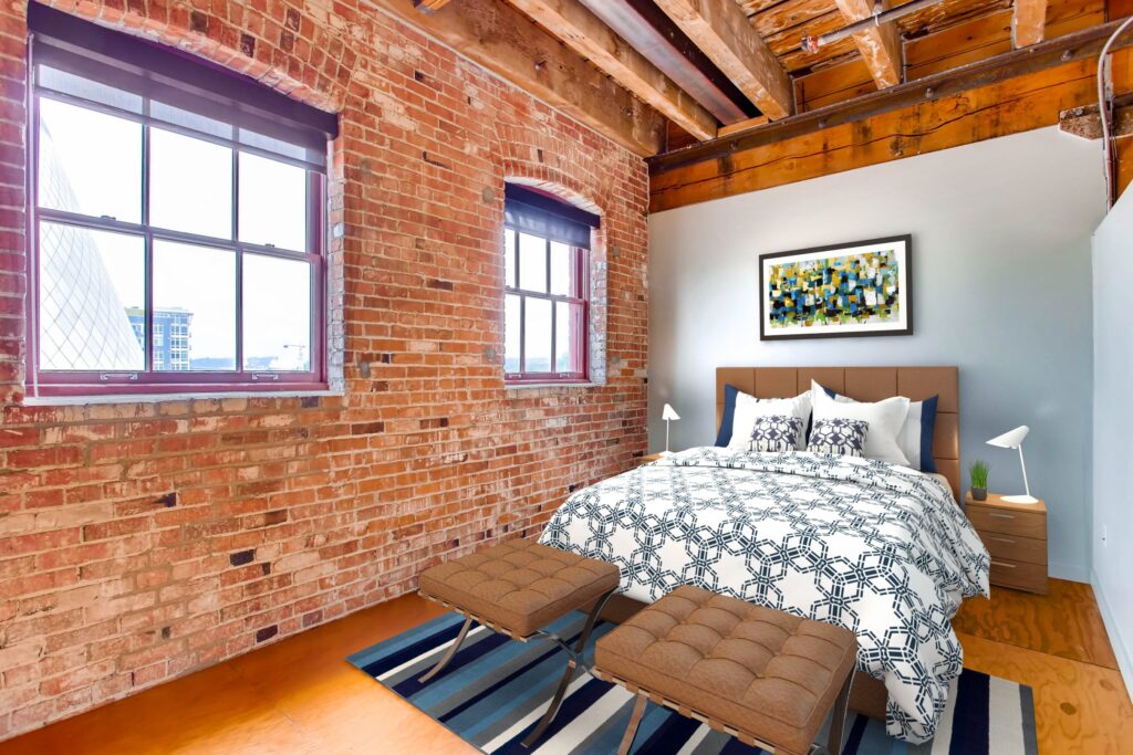 Bedroom with colorful pillows, large wall-art overhead, bedside tables and large windows